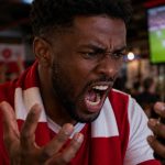 Angry Black football fan shouting at his smartphone while watching a match in a sports bar