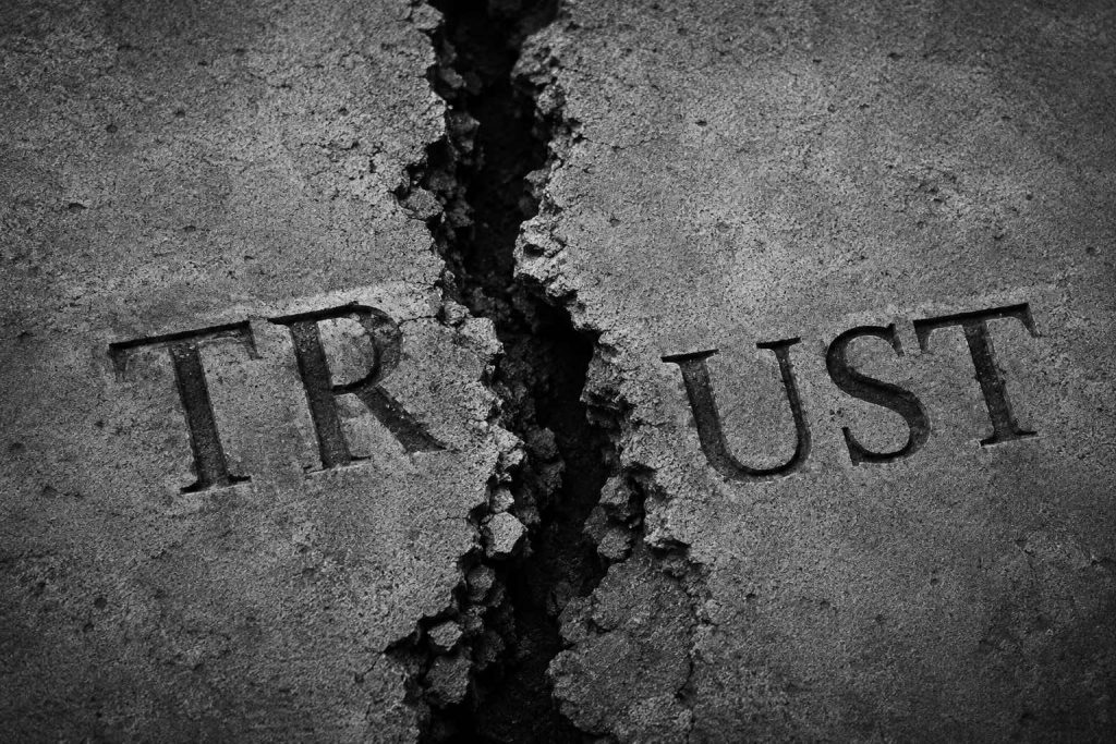 Cracked concrete surface with the word “TRUST” split apart by a deep fracture running through the center.